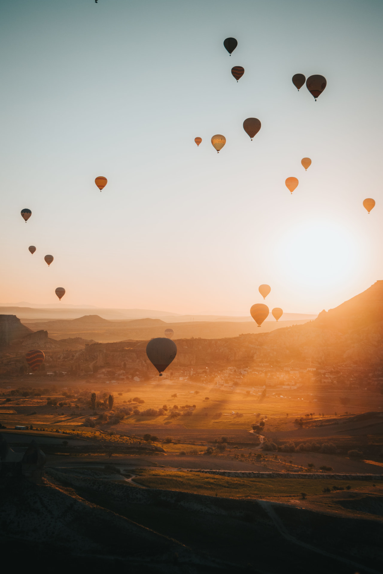 Hot-air balloons rising over a sunlit valley at dawn